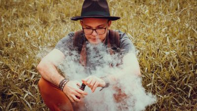 Jugendlicher mit Hut sitzt auf dem Boden und raucht Vape umhüllt von einer Rauchwolke. Bild: Pexels
